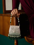 A hand holds an ornate 925 silver handbag with intricate nakaashi, green and white beaded fringe, and a pearl-and-green beaded strap, set against a warm wooden interior background.